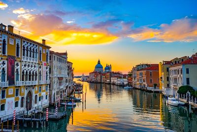 Boats in canal amidst buildings against sky during sunset