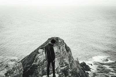 Rear view of woman standing on rock by sea