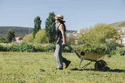 Farm worker wearing hat pulling wheelbarrow in field