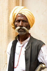 Senior man wearing turban standing against wall