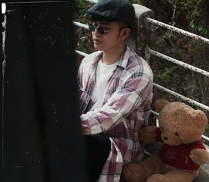 Thoughtful young man with teddy bear sitting on footbridge