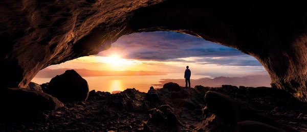 Silhouette man standing on rock formation at sunset