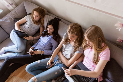 High angle view of teenage girls using technologies while watching tv in living room