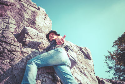 Low angle view of young man on rock against sky