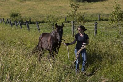 Smiling young woman with horse walking on grassy field