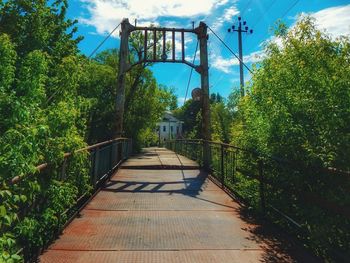 Footbridge amidst trees against sky