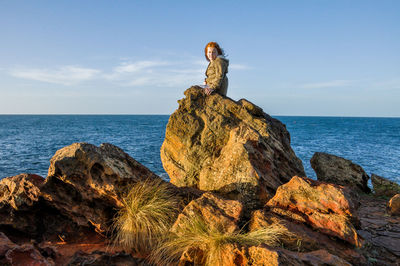 Girl sitting on rock by sea against sky