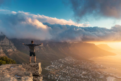 Rear view of man standing with arms outstretched on mountain against sky during sunset