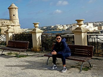 Full length of man sitting on bench in city