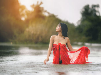 Young woman looking away against blurred water