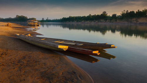 Boats moored in calm lake against sky on sunny day