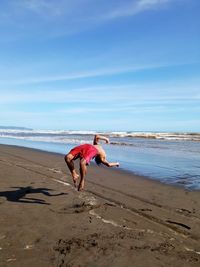 Young man jumping at beach against sky