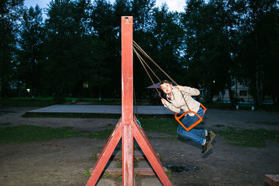 Beautiful young girl energetically and with pleasure swings on the swing at dusk.