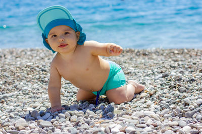 Full length of shirtless boy on pebbles at beach