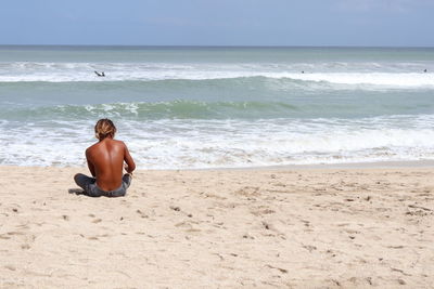 Full length of shirtless man sitting on beach