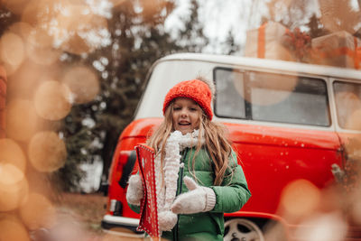 Cute smiling girl standing against car during winter