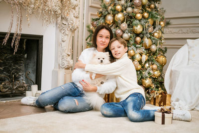 Happy family, mom and son. they are sitting near a christmas tree with a dog.