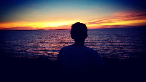 Silhouette woman sitting by sea against sky during sunset