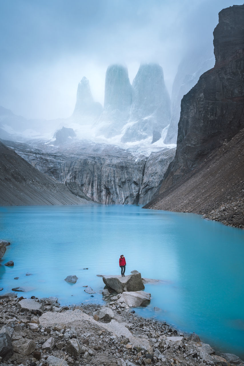 REAR VIEW OF PERSON IN LAKE BY MOUNTAINS