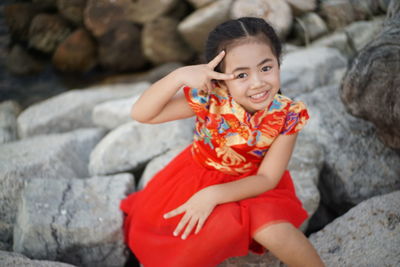 Portrait of smiling girl gesturing on forehead while sitting on rock