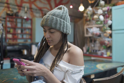 Young woman sitting in kitchen typing on her smartphone