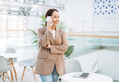 Adult smiling brunette business woman forty years in beige suit and jeans working on laptop 