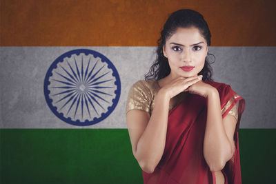 Portrait of smiling woman wearing maroon sari standing against indian flag