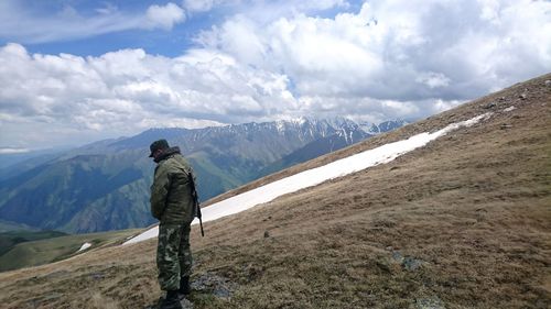 Side view of army officer standing on mountain against cloudy sky