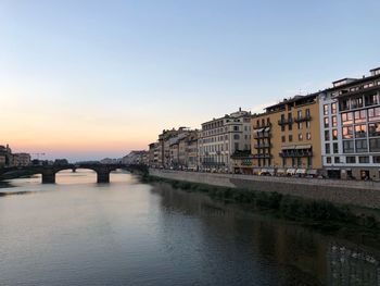 Bridge over river by buildings against sky during sunset