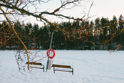 Empty bench on snow covered field against sky