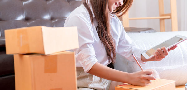 Midsection of woman holding mobile phone while sitting in box