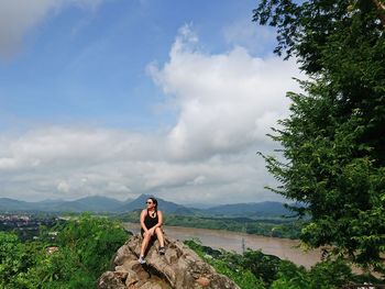 Woman sitting on rock against sky