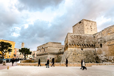 People at historical building against cloudy sky