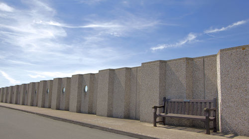 Wall by empty bench against sky