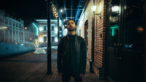 Portrait of young man standing in city at night