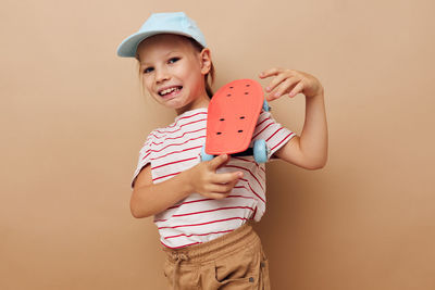 Portrait of girl holding skateboard against beige background