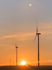 Wind turbines on field against sky during sunset