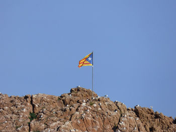 Low angle view of flag waving on rock against clear sky