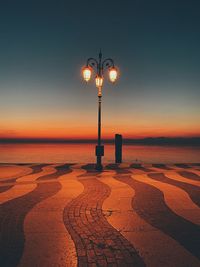 Street light on beach against sky at sunset