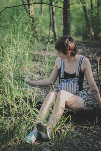 Full length of young woman sitting on field by plants in forest
