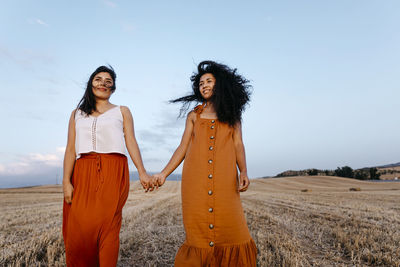Smiling young female friends holding hands while standing in farm