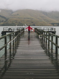 Woman on a red jacket happily running at port levy jetty, nz