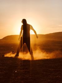 Silhouette man standing on landscape against sky during sunset