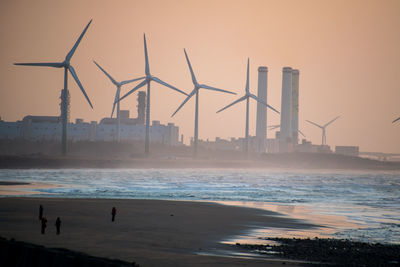 Windmills on beach against sky during sunset