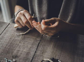 Close-up midsection of woman making bracelets at table