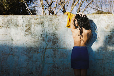 Rear view of shirtless woman standing against wall