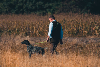 Rear view of man walking with dog on field