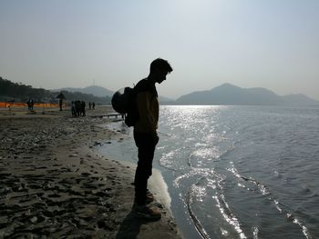 Side view of man standing at beach against clear sky