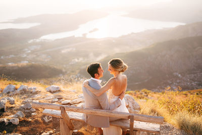 Couple sitting on mountain against sky