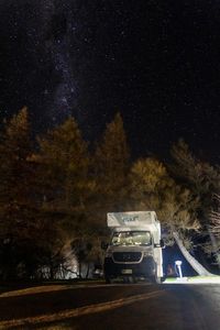 Car on road by trees against sky at night